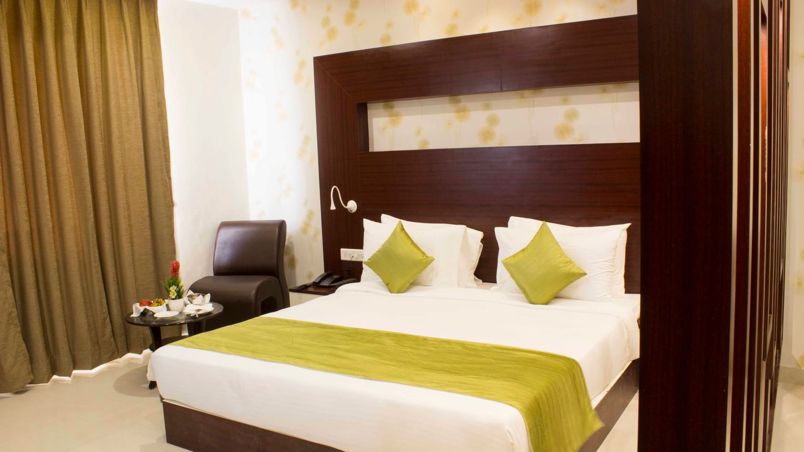 A hotel bedroom with a large bed, elegant wooden headboard, and green bed runner | Daksh Suite | Daksh The Madhuvan Suites