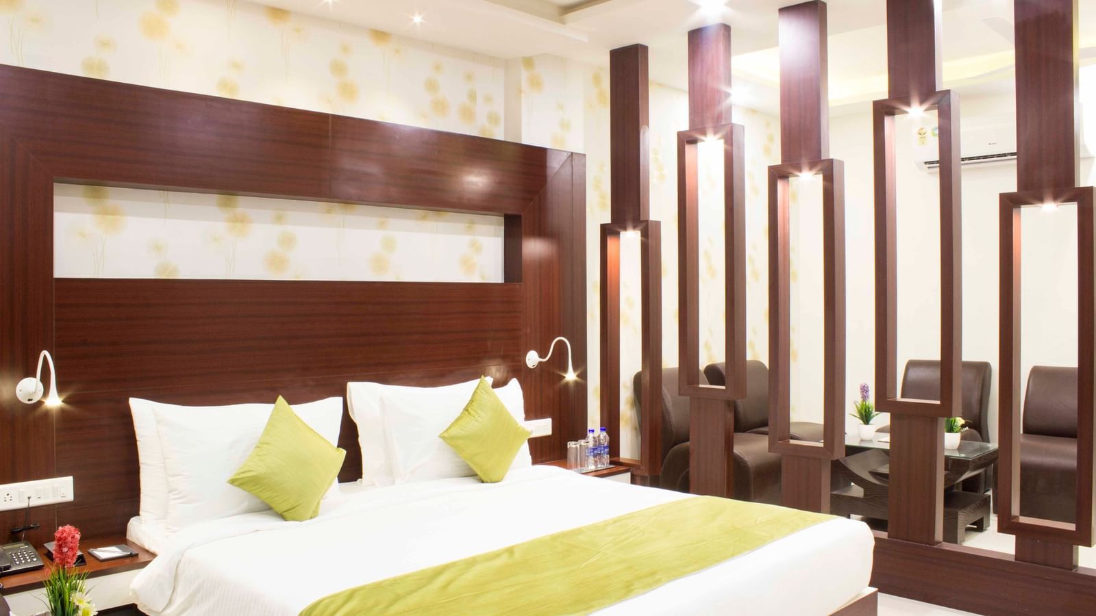 A modern hotel bedroom with a bed, green bed runner, and dark wood paneling | Daksh Suite | Daksh The Madhuvan Suites