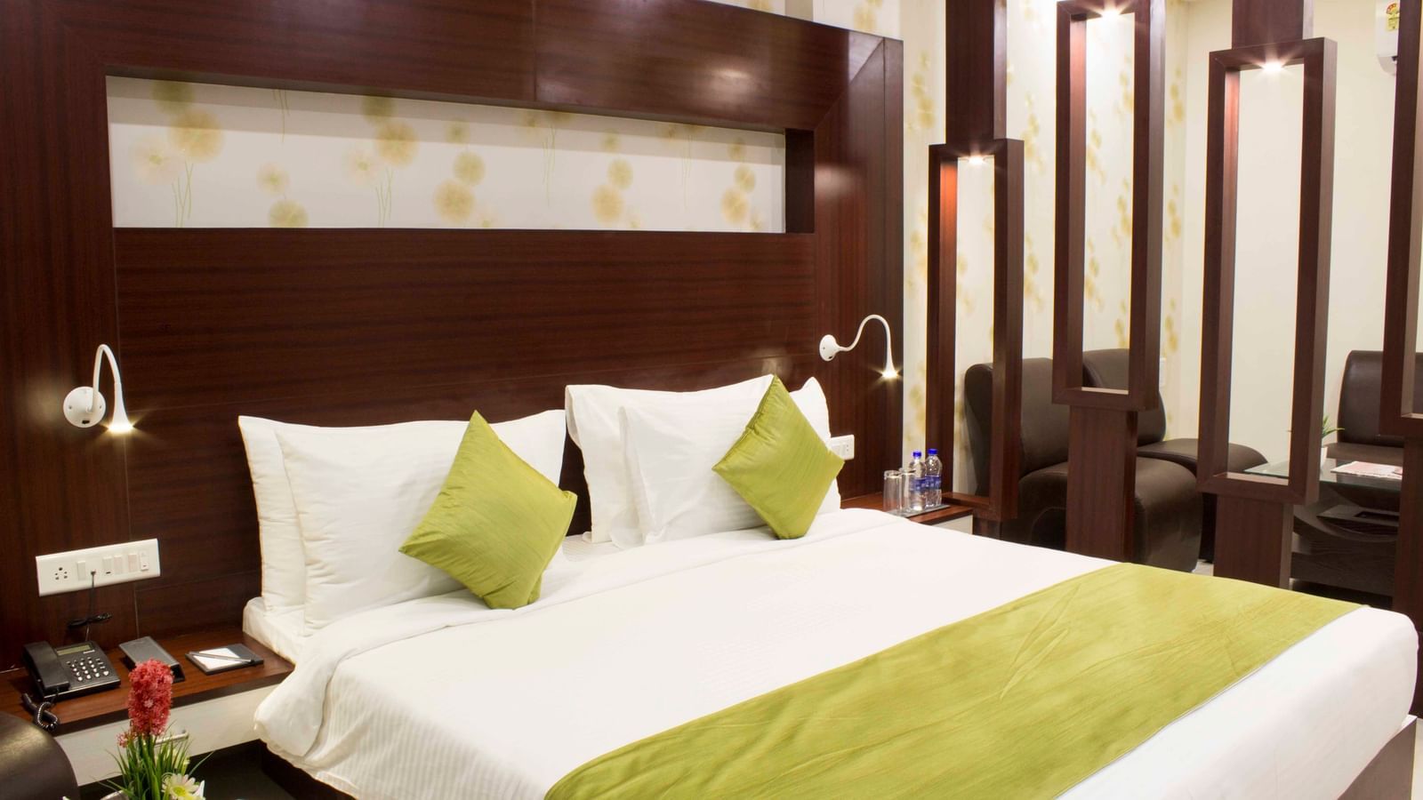 A modern hotel bedroom with a bed, green bed runner, and dark wood paneling | Daksh Suite | Daksh The Madhuvan Suites