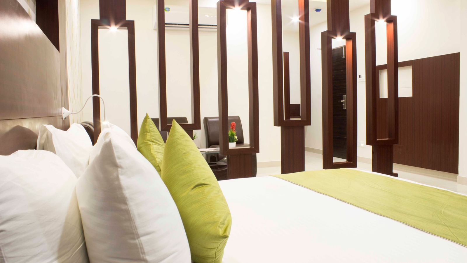 A close-up of a bed with white and green bedding and decorative pillows | Daksh Suite | Daksh The Madhuvan Suites