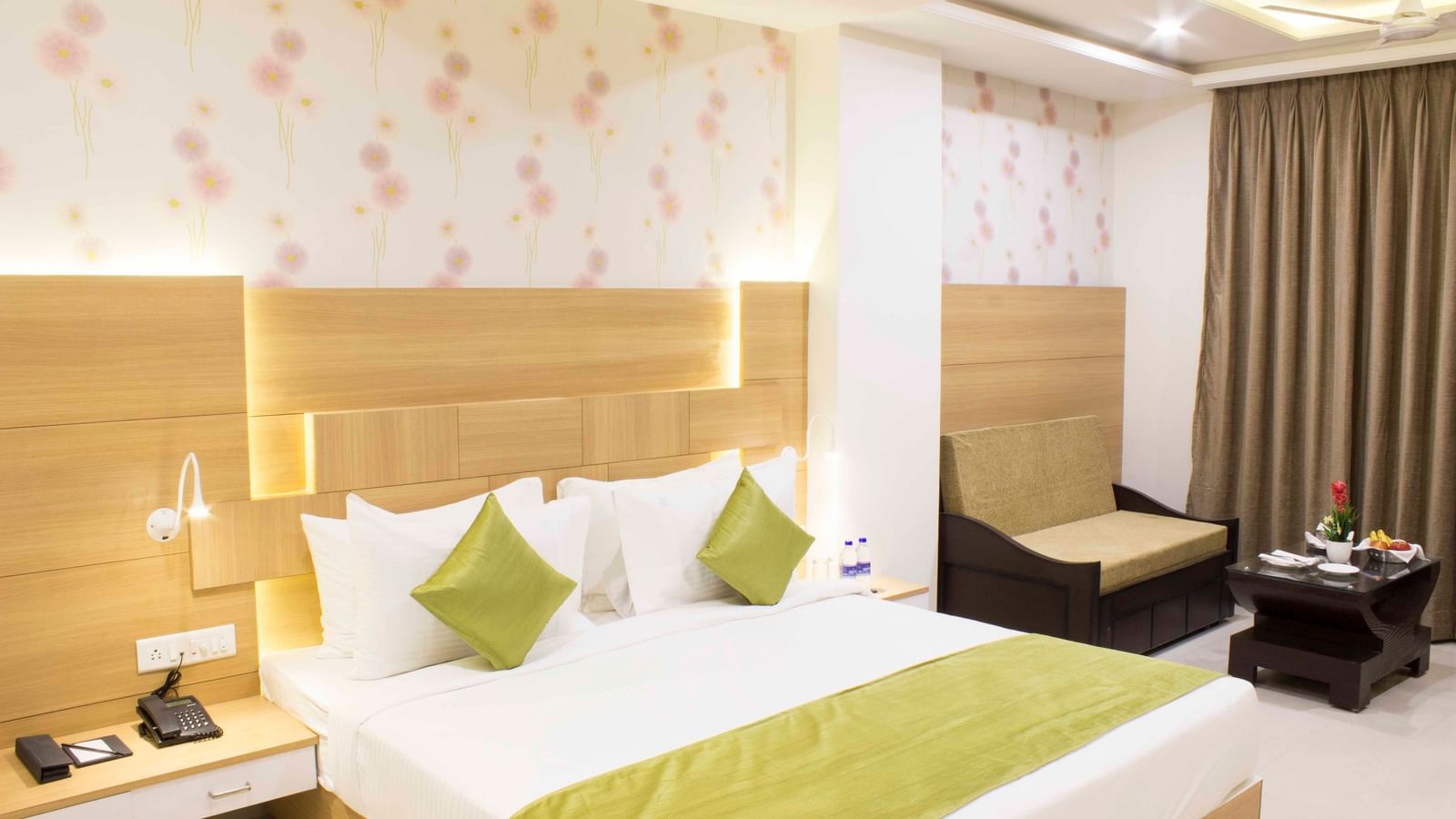 A hotel bedroom with a large bed, light wood headboard, and green bed runner | Daksh Pride Room | Daksh The Madhuvan Suites
