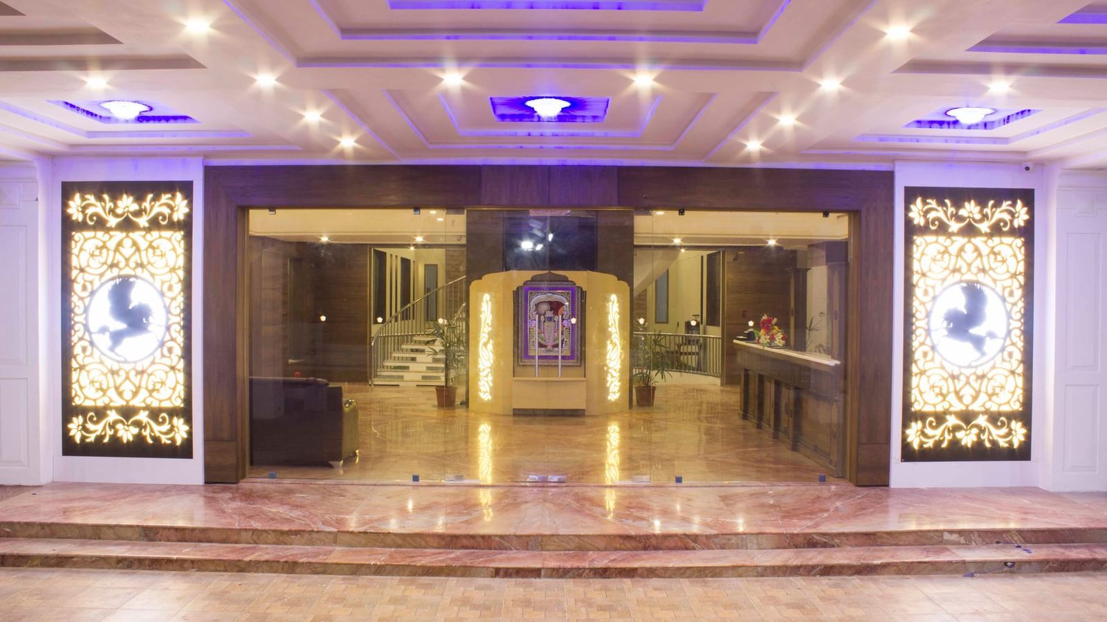 A brightly lit hotel lobby with intricate ceiling lights and columns | Daksh The Madhuvan Suites