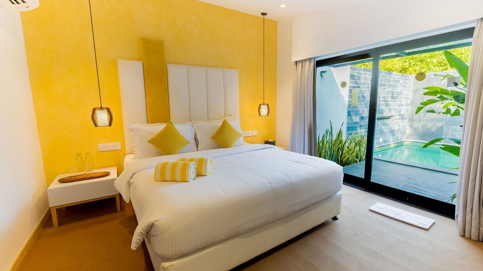 Pool Villa With Private Garden at Darza Resorts features a white bed with yellow cushions, a yellow accent wall, and a large sliding door revealing a private plunge pool