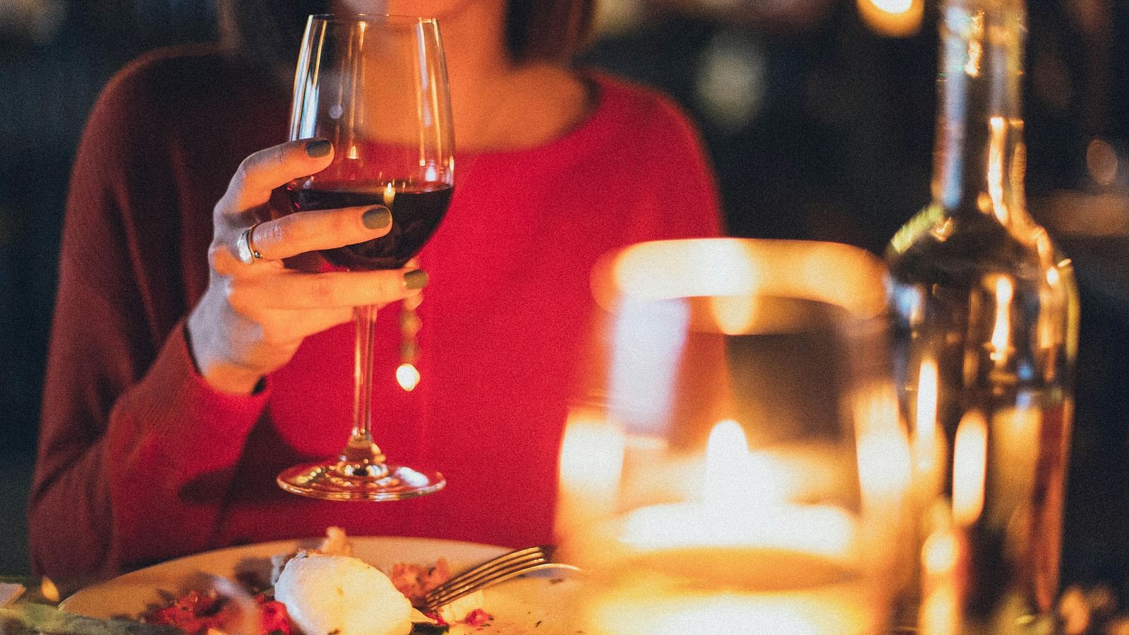 a woman holding a wine glass while sitting for dinner at a candle lit dinner table