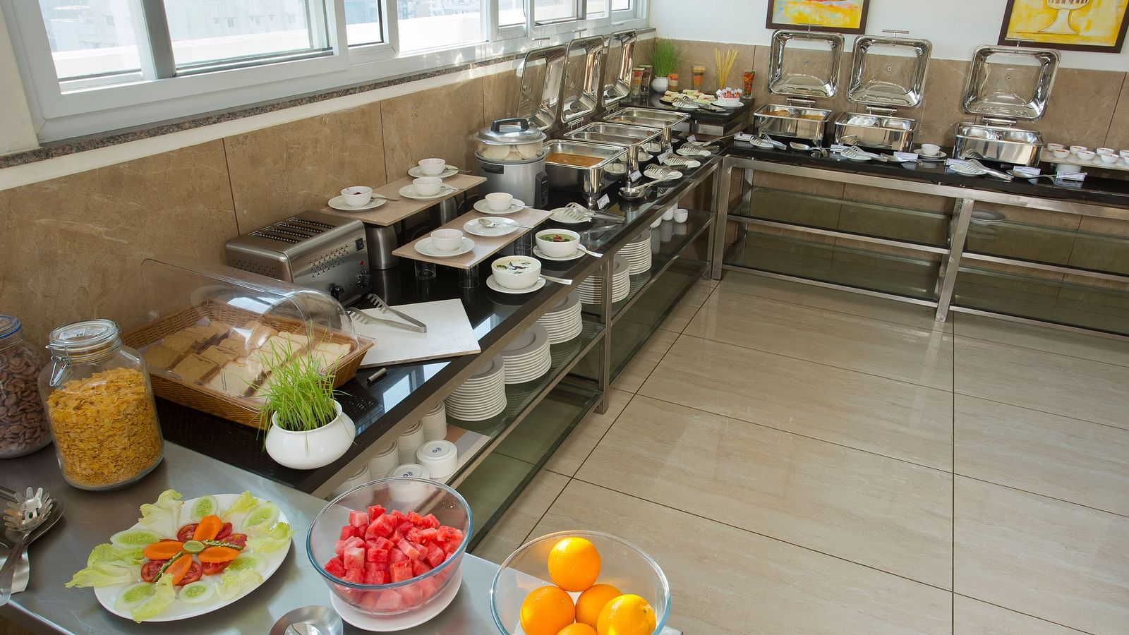 A hotel breakfast buffet with a variety of food items on display near a window with a city view - De Venetian by TGI, Brookefield