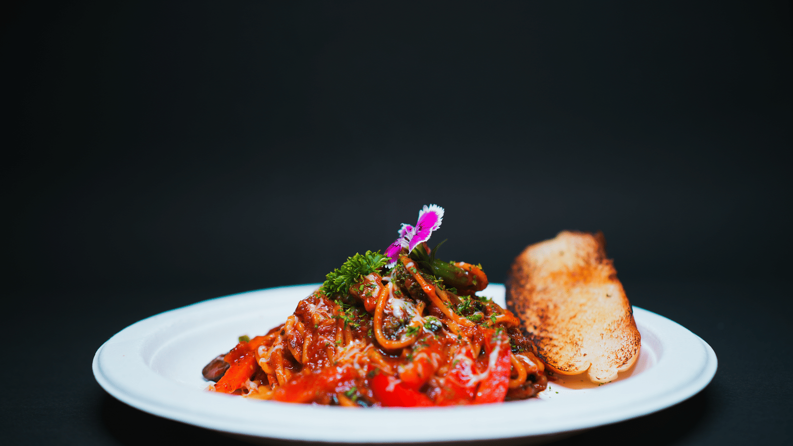 A gourmet pasta dish topped with rich tomato sauce, herbs, and an edible flower, served with a bread roll at D Café in Dip Holidays.