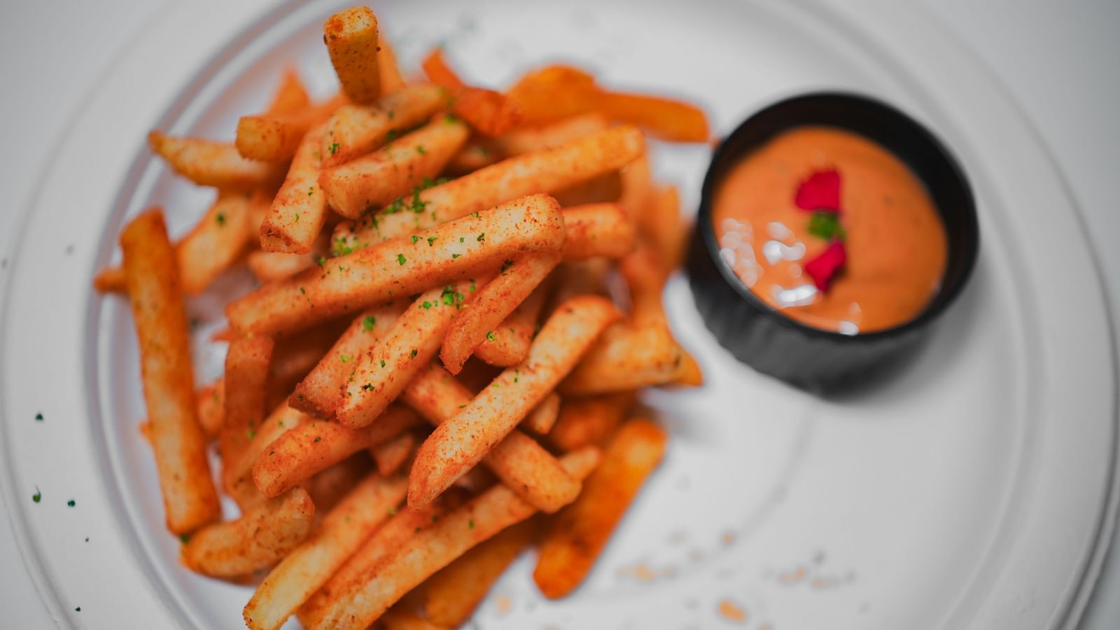 A plate of crispy seasoned French fries served with a side of creamy dipping sauce, garnished with herbs, at D Café in Dip Holidays.