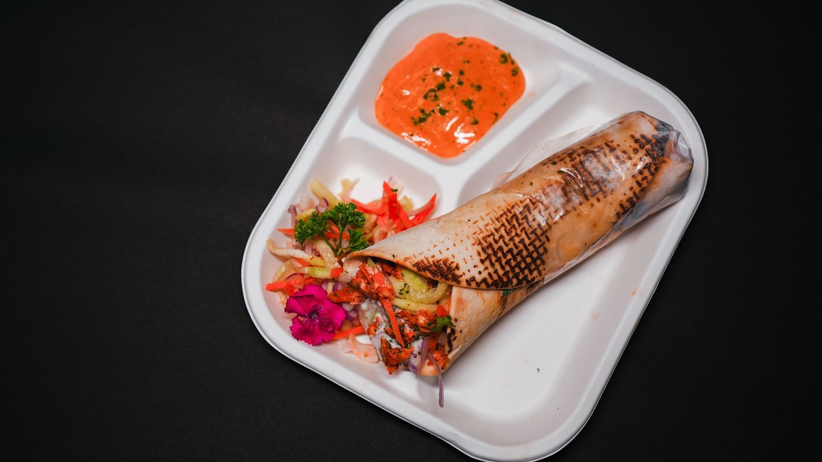 A grilled wrap with fresh salad and dipping sauce, beautifully plated on a white tray at D Café in Dip Holidays.
