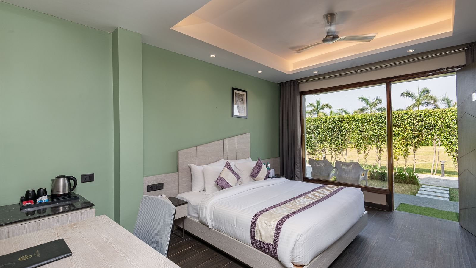 A spacious room at DLS Forest Vines Resort, complete with a large bed, bedside table, table and chairs, and a glass door opening to the balcony.