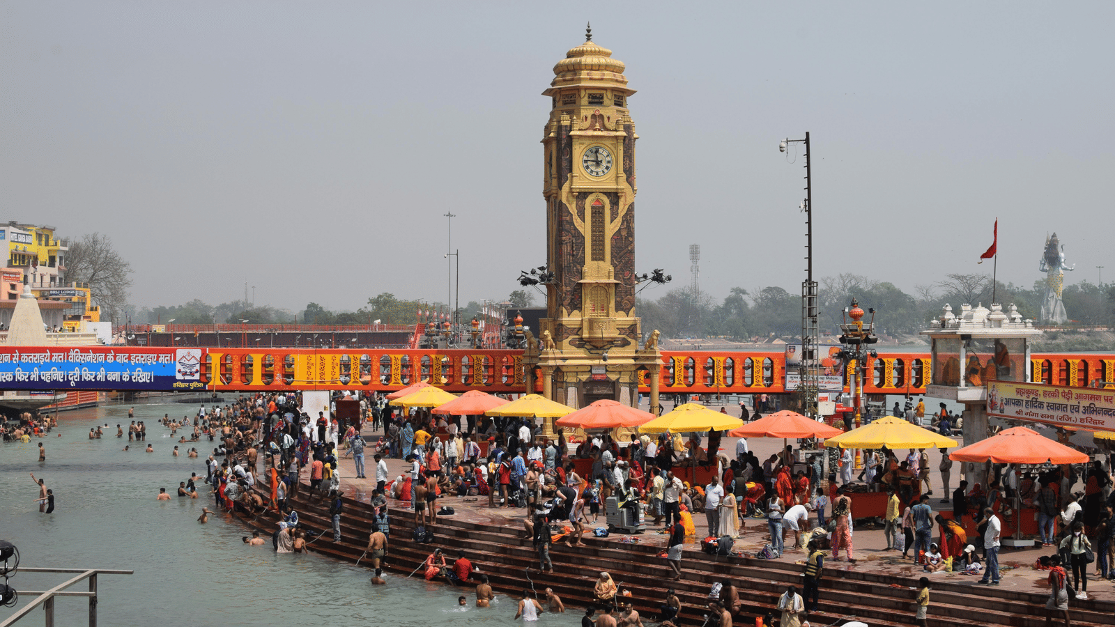 A view of the Ganga ghat with a huge number of crowd gathered and a clock tower in the background