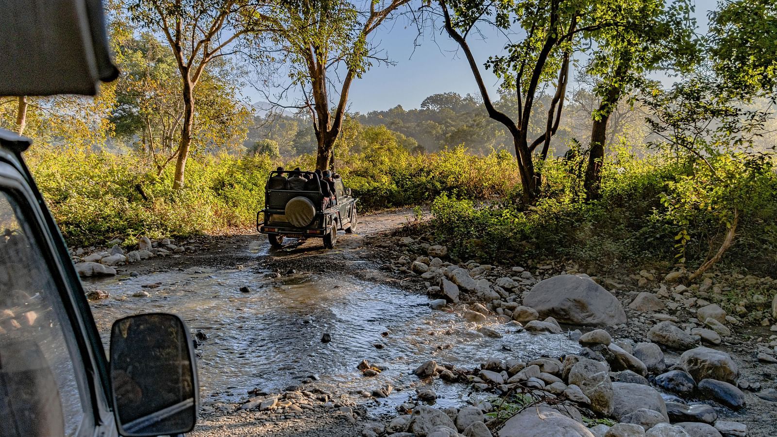 image of two safari jeeps traversing through a stony water stream at Jim Corbett