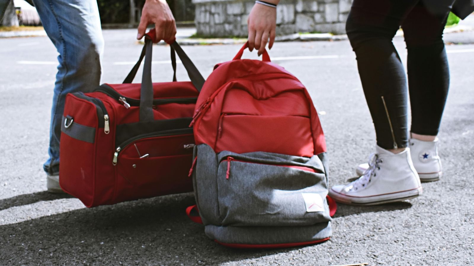 2 people standing on the road with bags, holding luggage.