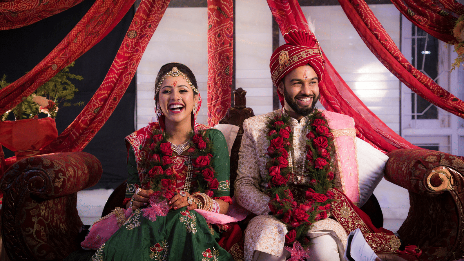 A close up of a indian couple sitting on a couch during their wedding with aesthetically pleasing decor.