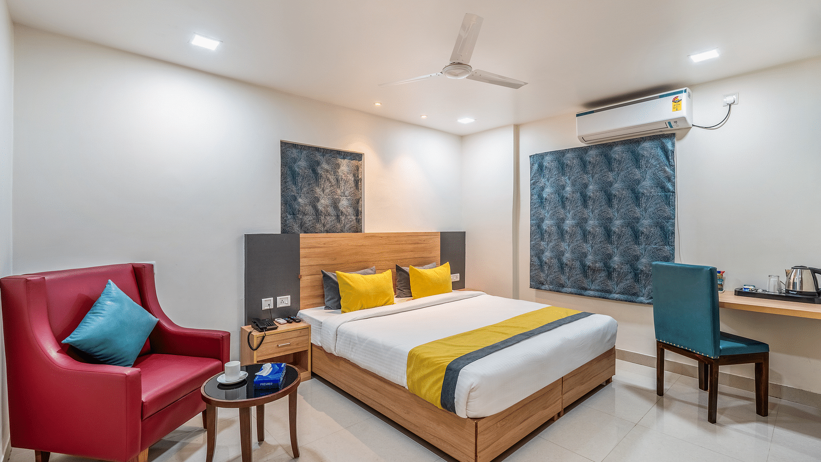 Shot of a bed in a room at the hotel, a red single couch, a small tea table and a study table | AIG Hospital near hotel Eminent Suites & Apartments, Hi-Tech City