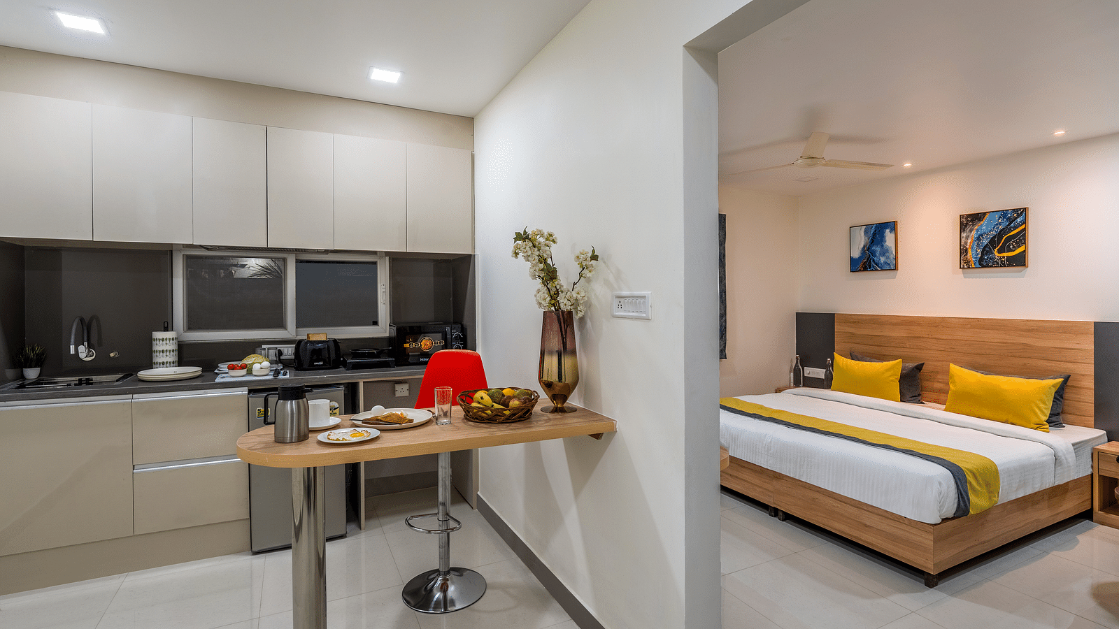 A shot of an apartment in our hotel that showcases the open modular kitchen with a table and a part of the bedroom featuring a king size bed | Eminent Suites & Apartments, Hi-Tech City