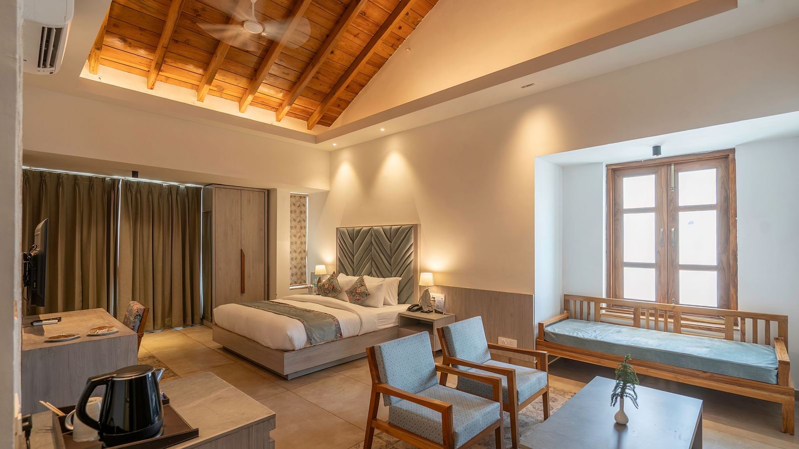 A spacious hotel room with a king size bed, a seating area, and a view of the lush green outdoors.