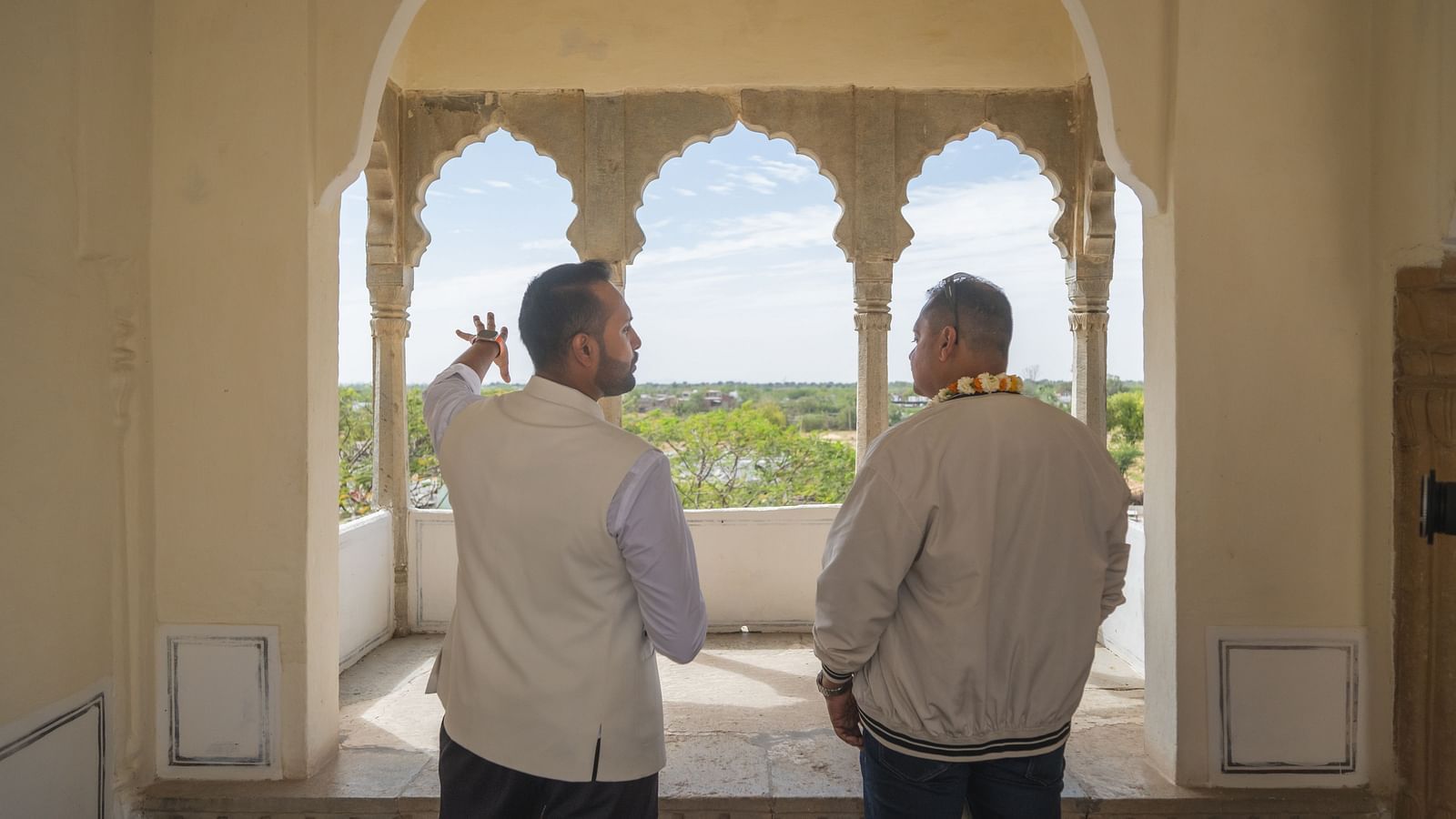 Two individuals stand in an arched opening, looking out at the landscape from Fort Barli, Ajmer.