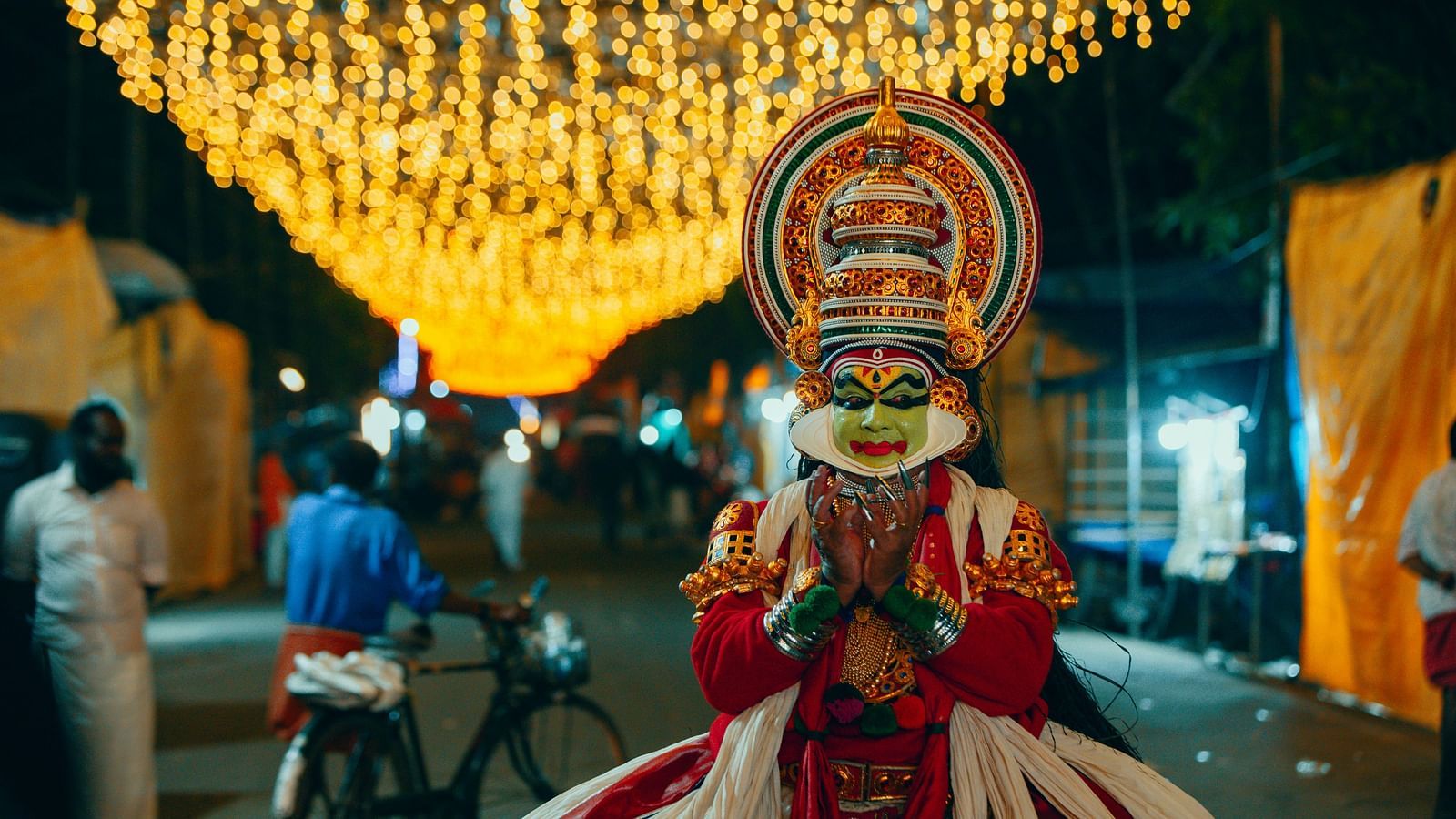 A person dressed in Kathakali costumes, striking poses near a lamp.
