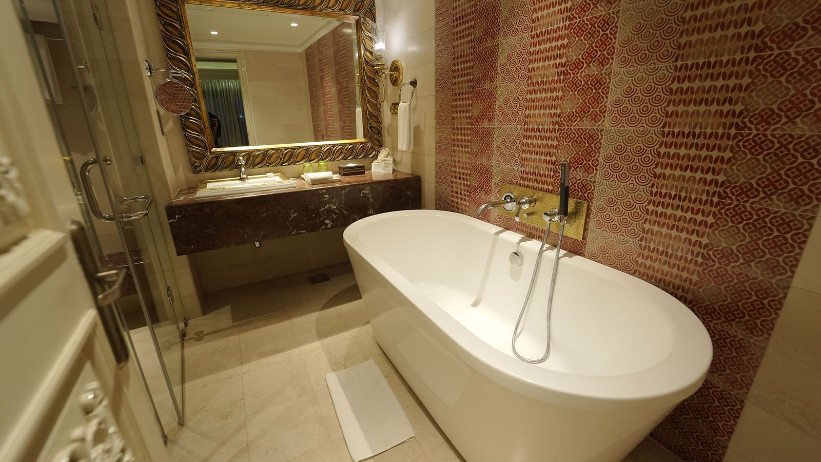 Fragrant Nature Cochin bathroom featuring a freestanding bathtub, ornate mirror, and red-patterned tiled wall.