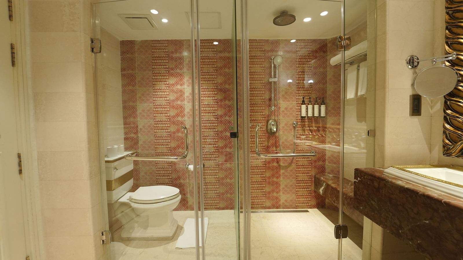 A bathroom at Fragrant Nature Cochin featuring a glass-enclosed shower and toilet with patterned red tiles and modern fittings.