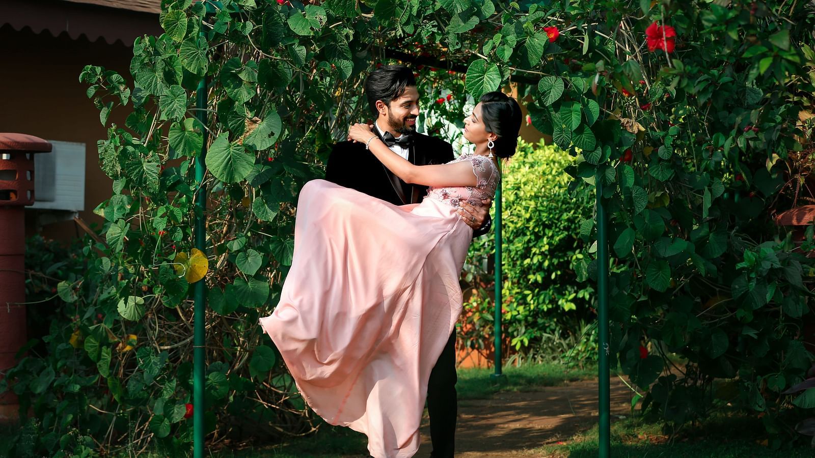 A couple’s wedding photoshoot with the groom carrying the bride through the garden.