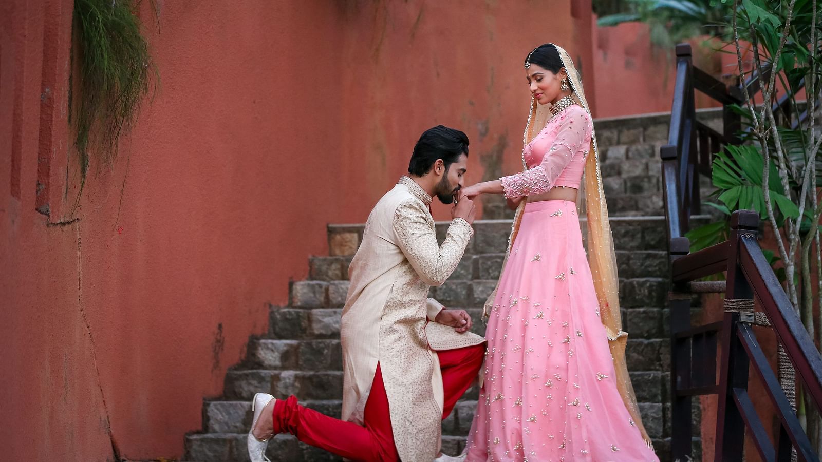 A couple’s wedding photoshoot by the staircase with the groom on one knee