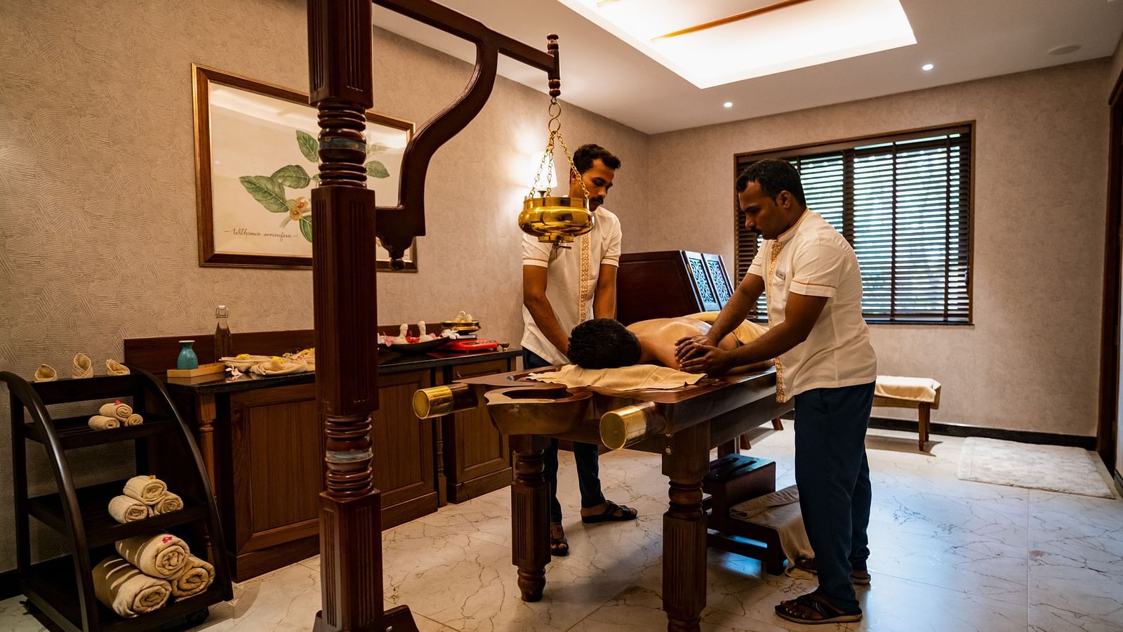 Two masseurs performing Abhyanga on a guests who is sleeping face down on a massage table - Gamyam Resort