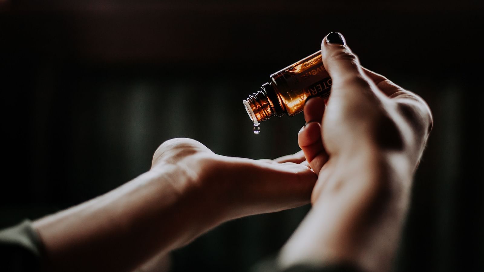 a person pouring essential oil by the drop on to the palm of their hand