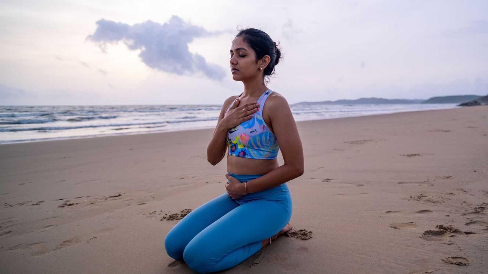 A woman sitting beside an ocean in a yoga pose