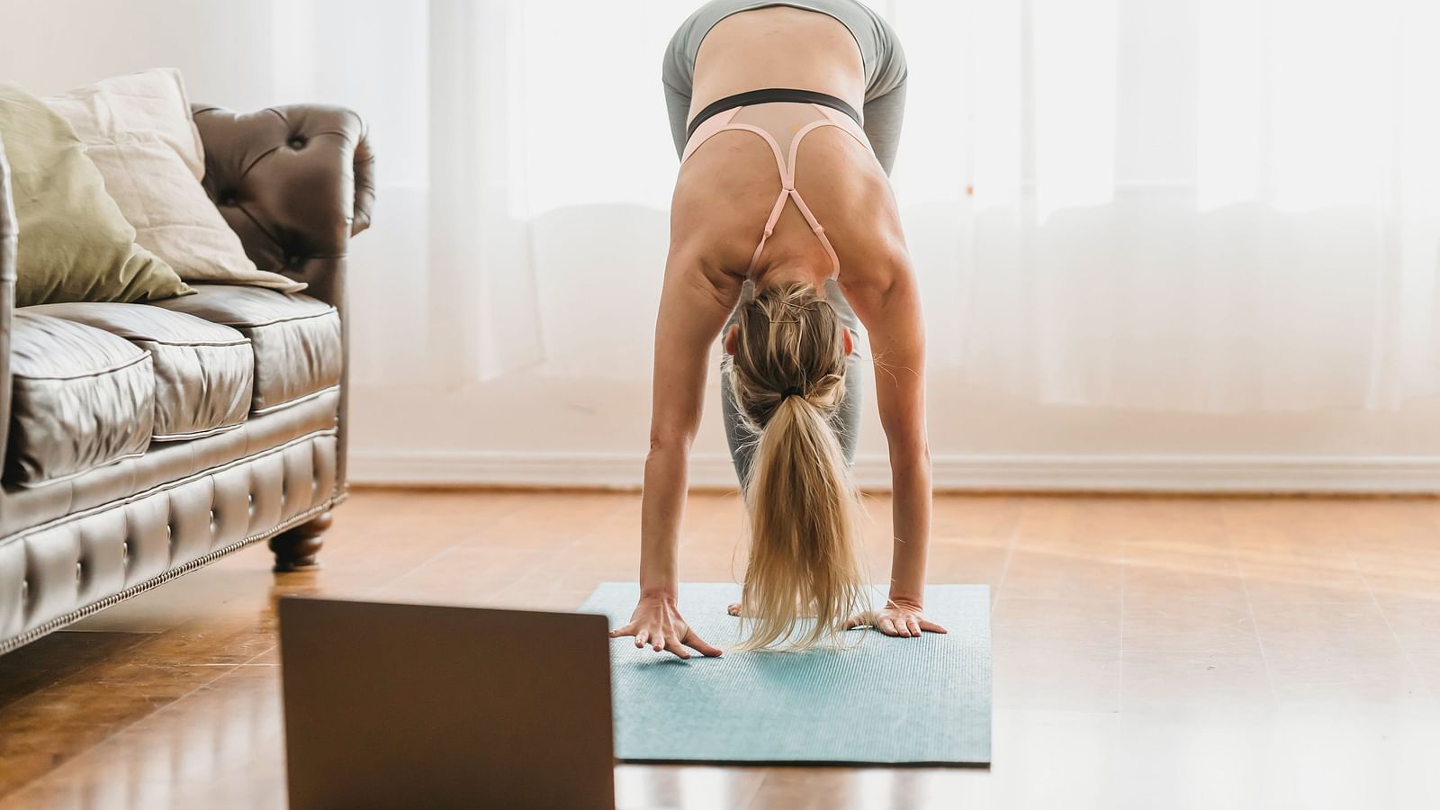 A woman performing a yoga asana in her room with a laptop in front of her and a sofa next to her