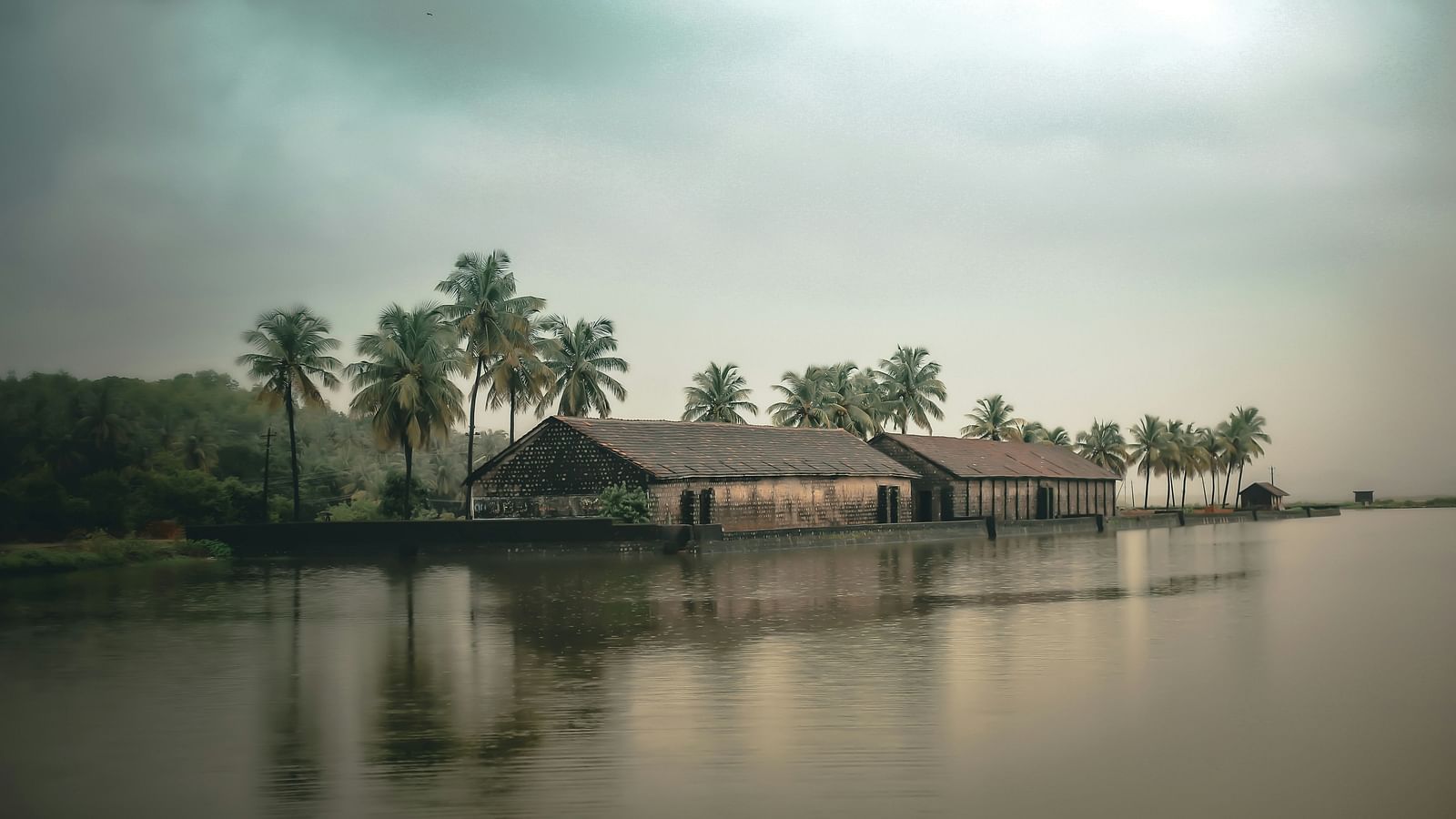 Two houses on the banks of a river in Gokarna with coconut trees in the background