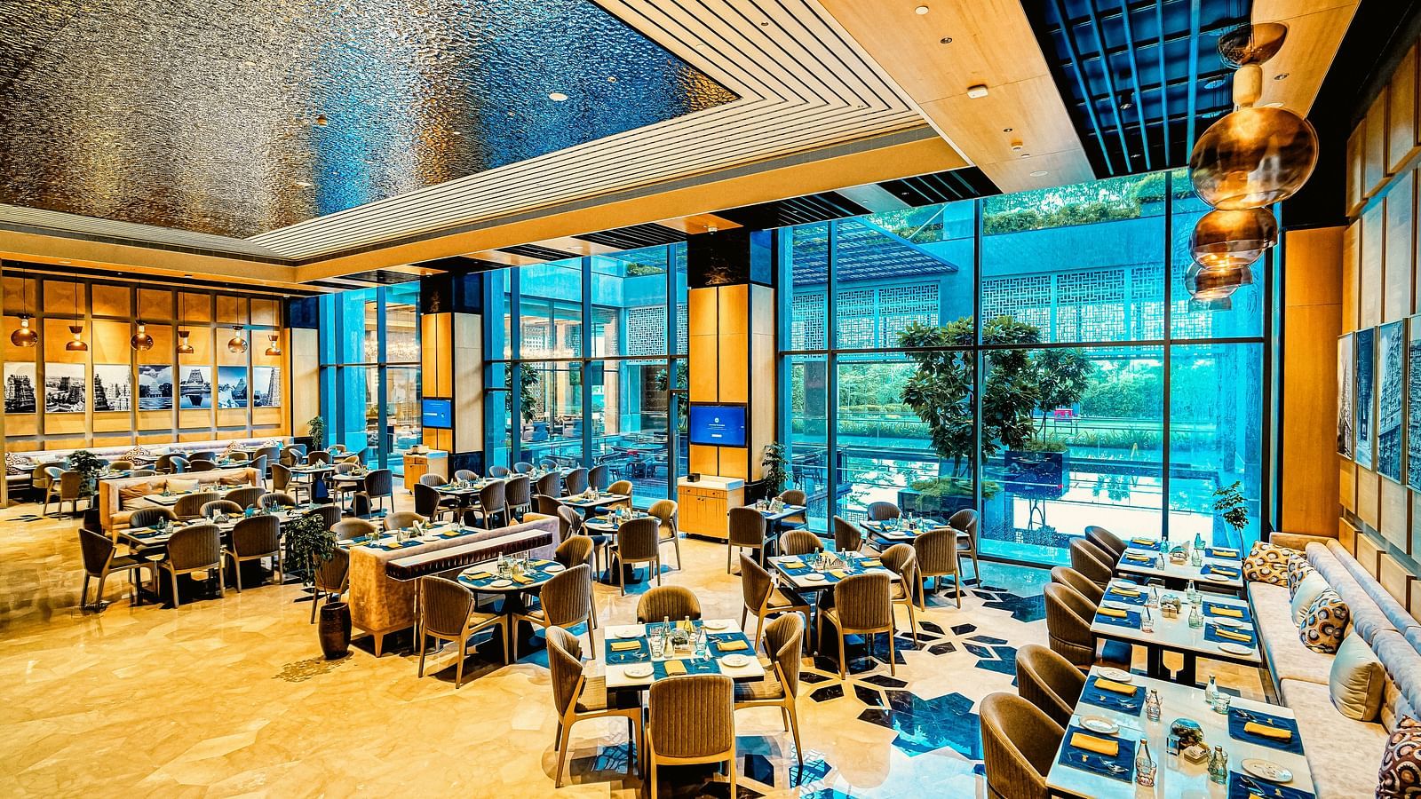 A bright and modern dining area with floor-to-ceiling windows, offering a relaxed and open atmosphere - Grand Madurai by GRT Hotels
