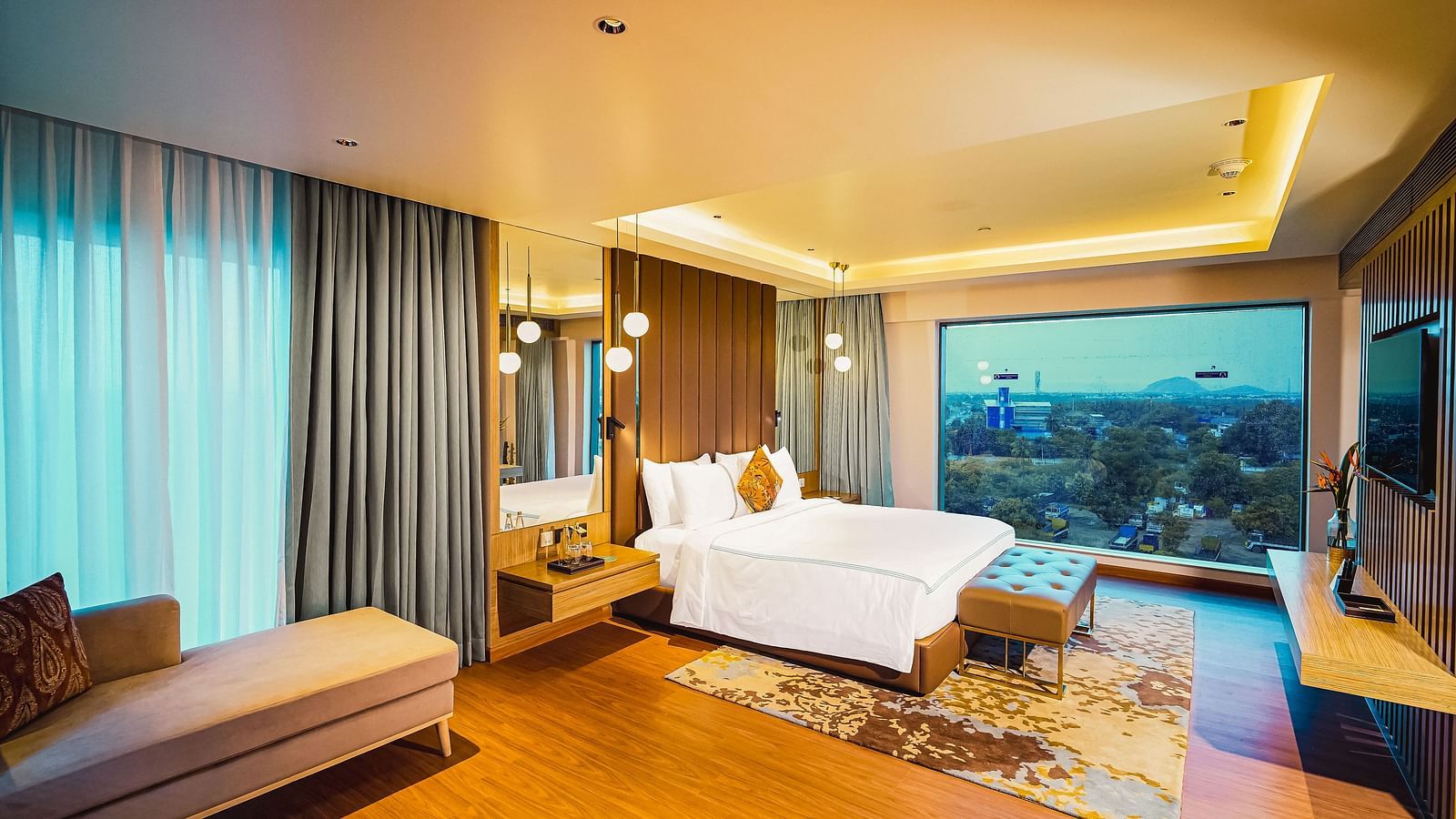 An elegant hotel room in Madurai with a large bed, a couch, a beautiful window view and a wall-mounted television - Grand Madurai by GRT Hotels
