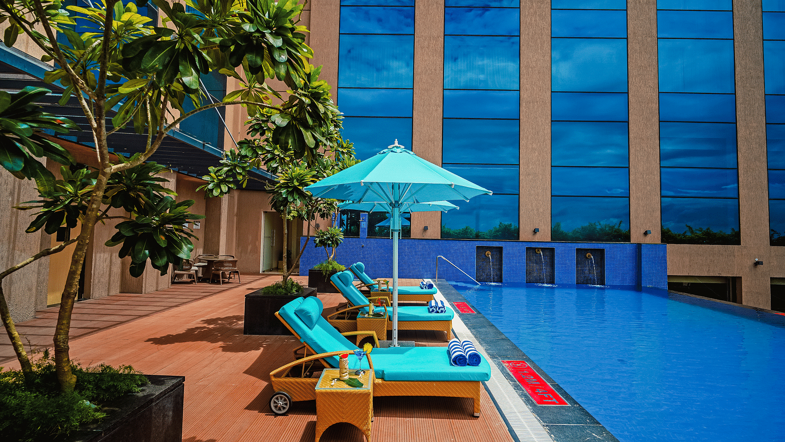 A daytime view of the pool with vibrant blue sun loungers and umbrellas, perfect for a tropical retreat - Grand Madurai by GRT Hotels