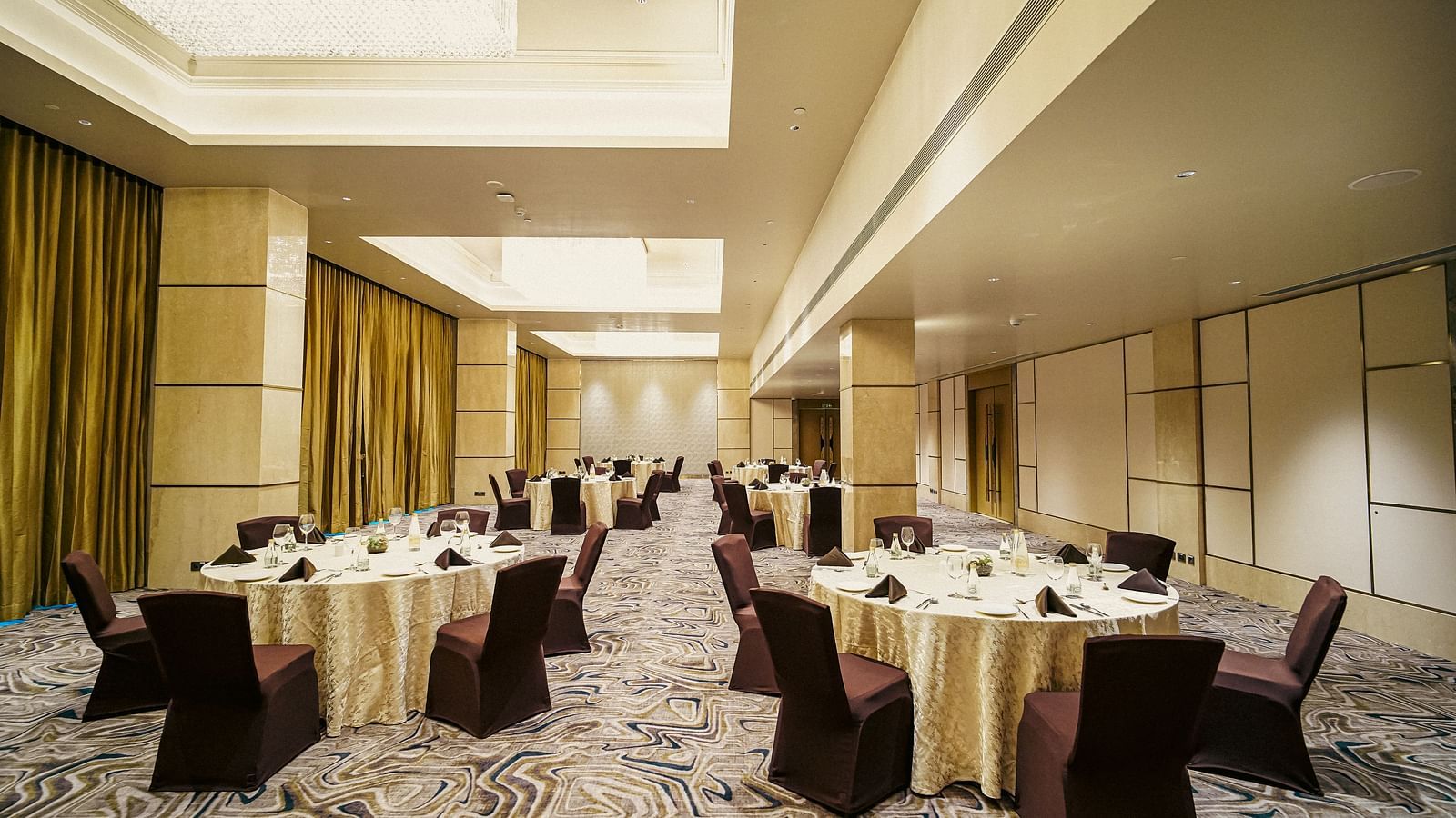 Our Banquet hall in Madurai with round tables, elegant chandeliers and warm lighting - Grand Madurai by GRT Hotels