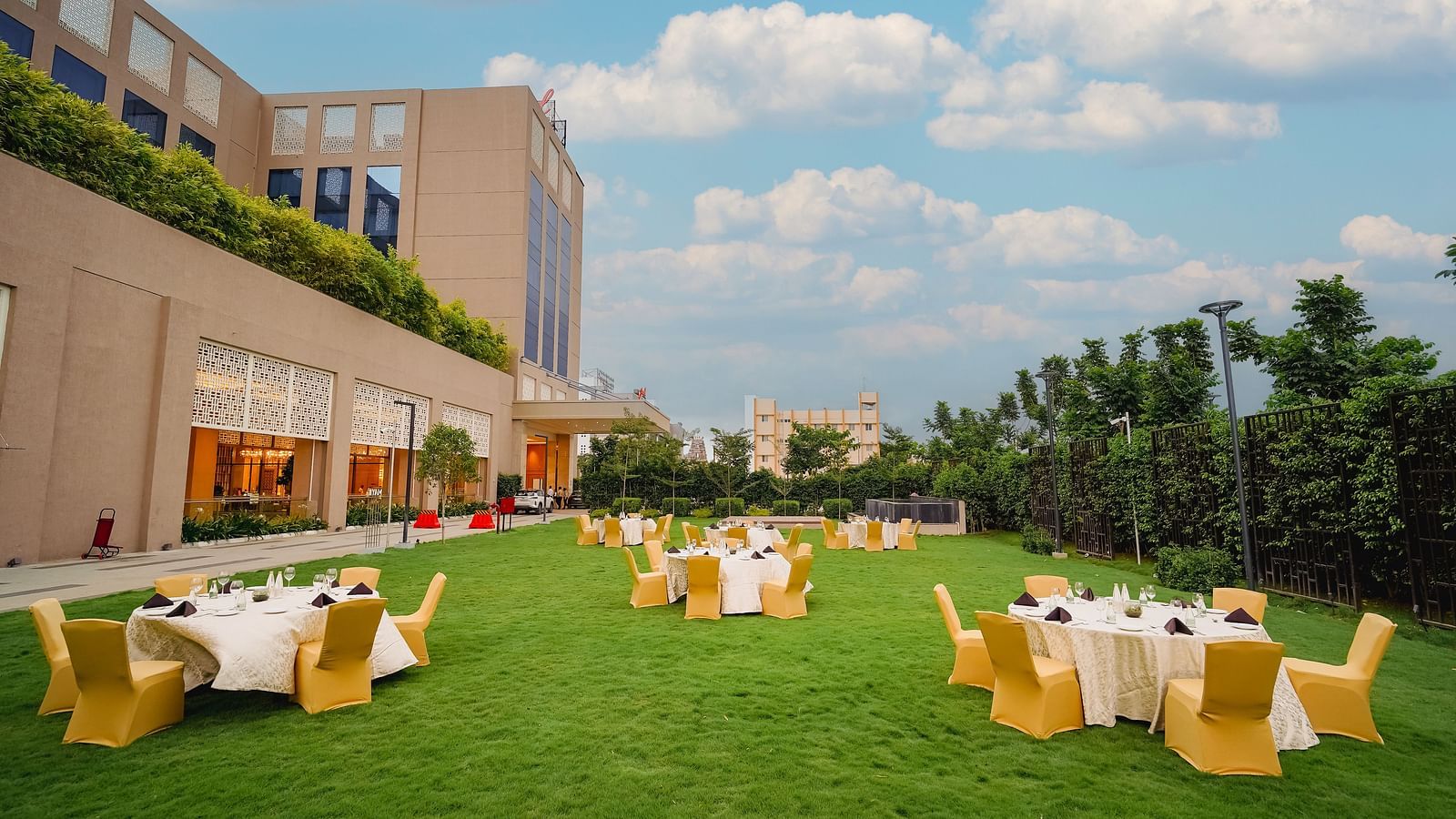 A beautifully manicured lawn with outdoor seating, perfect for events, surrounded by a hotel building - Grand Madurai by GRT Hotels