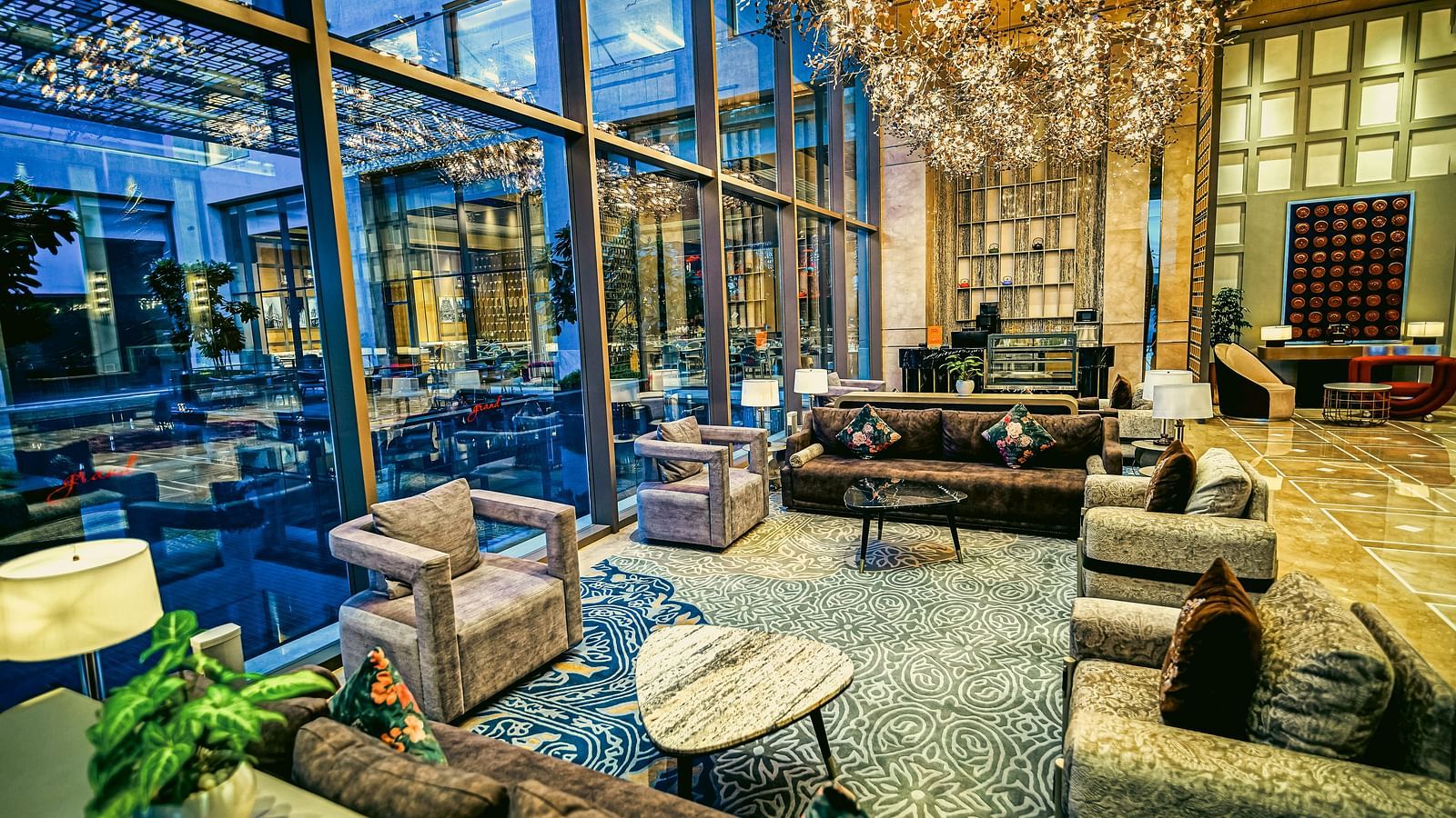 A modern hotel lounge with cosy seating, floor-to-ceiling windows, and artistic lighting features - Grand Madurai by GRT Hotels
