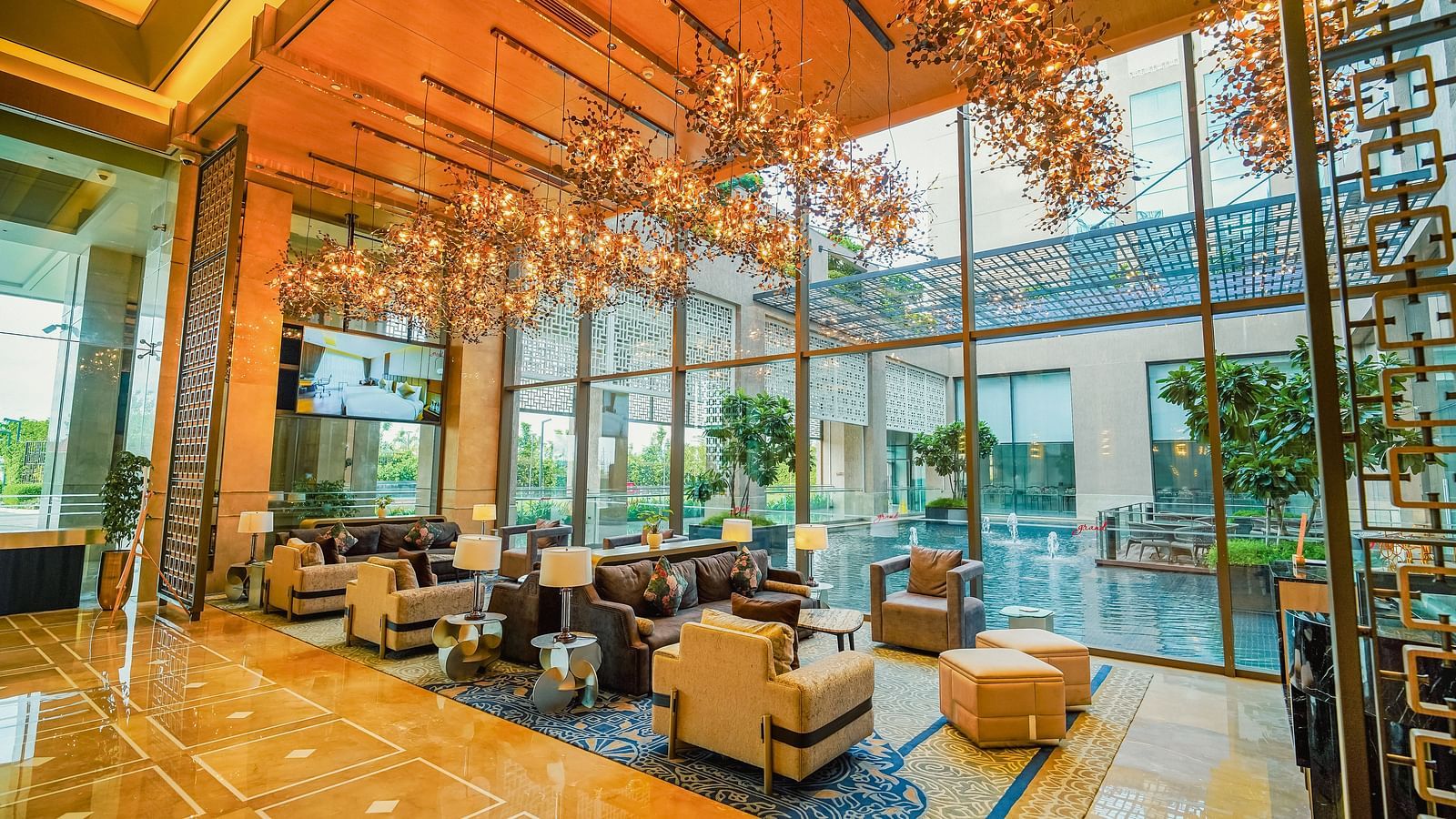 A comfortable hotel seating area with ample natural light from large windows and a vibrant chandelier - Grand Madurai by GRT Hotels