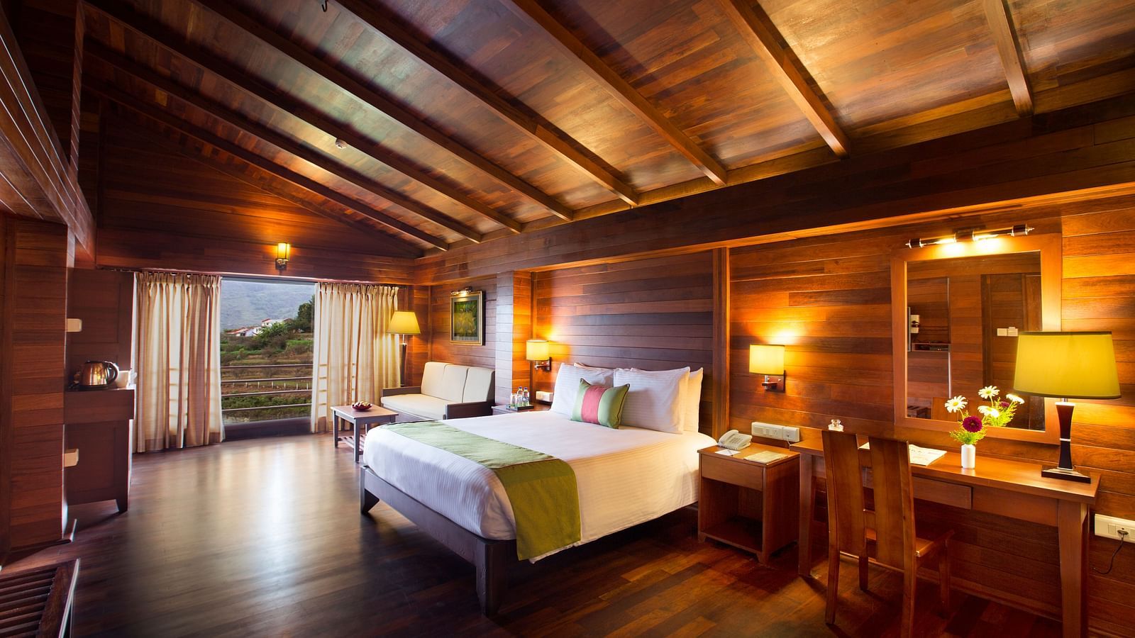 An image of Timber Charlet room with king size bed, bed side table, lamps, dressing table, chair, and bright lighting - GReaT Trails Kodaikanal By GRT Hotels