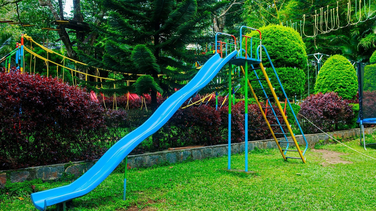 A brightly coloured blue slide in a lush green garden surrounded by neatly trimmed bushes and trees—an inviting outdoor play area at our child-friendly hotel in Yercaud, perfect for young guests to enjoy.