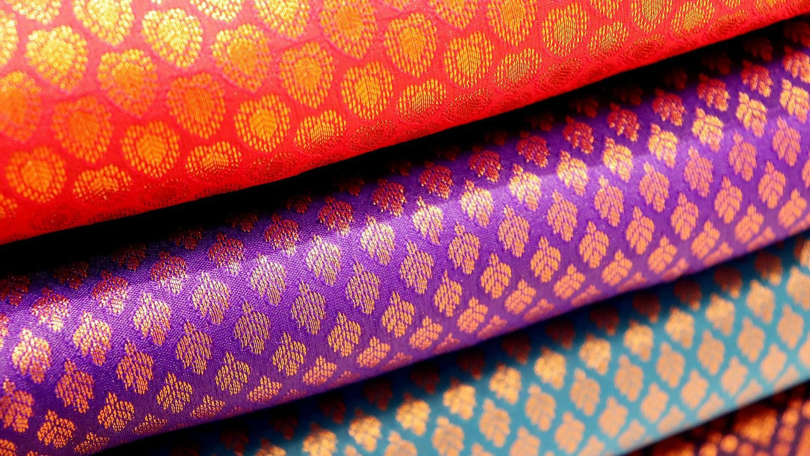 Vibrant Indian silk sarees stacked in shades of pink, purple, and gold.