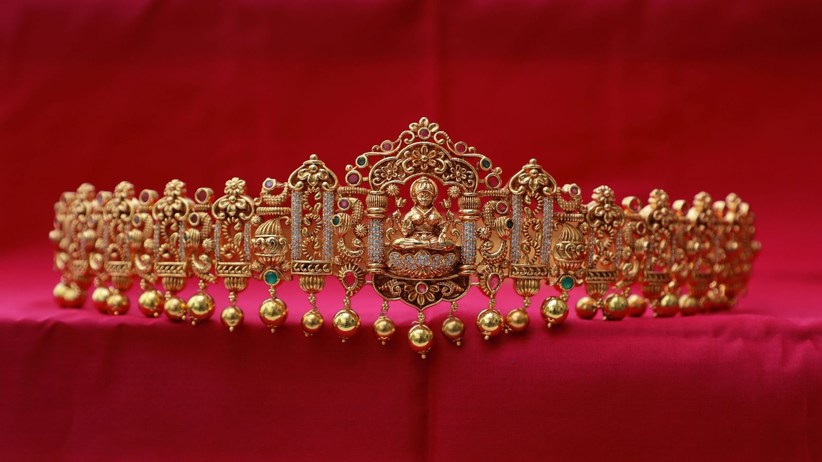 Elegant gold jewellery piece with intricate detailing, placed on red fabric.