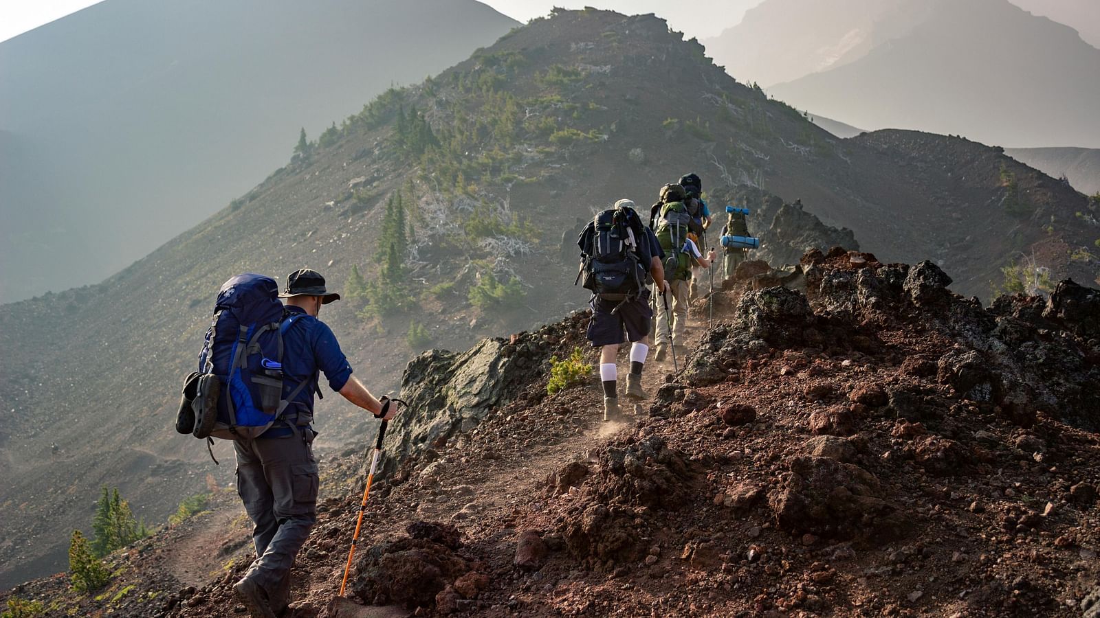 Group of hikers trekking along a mountain trail with misty peaks in the background.