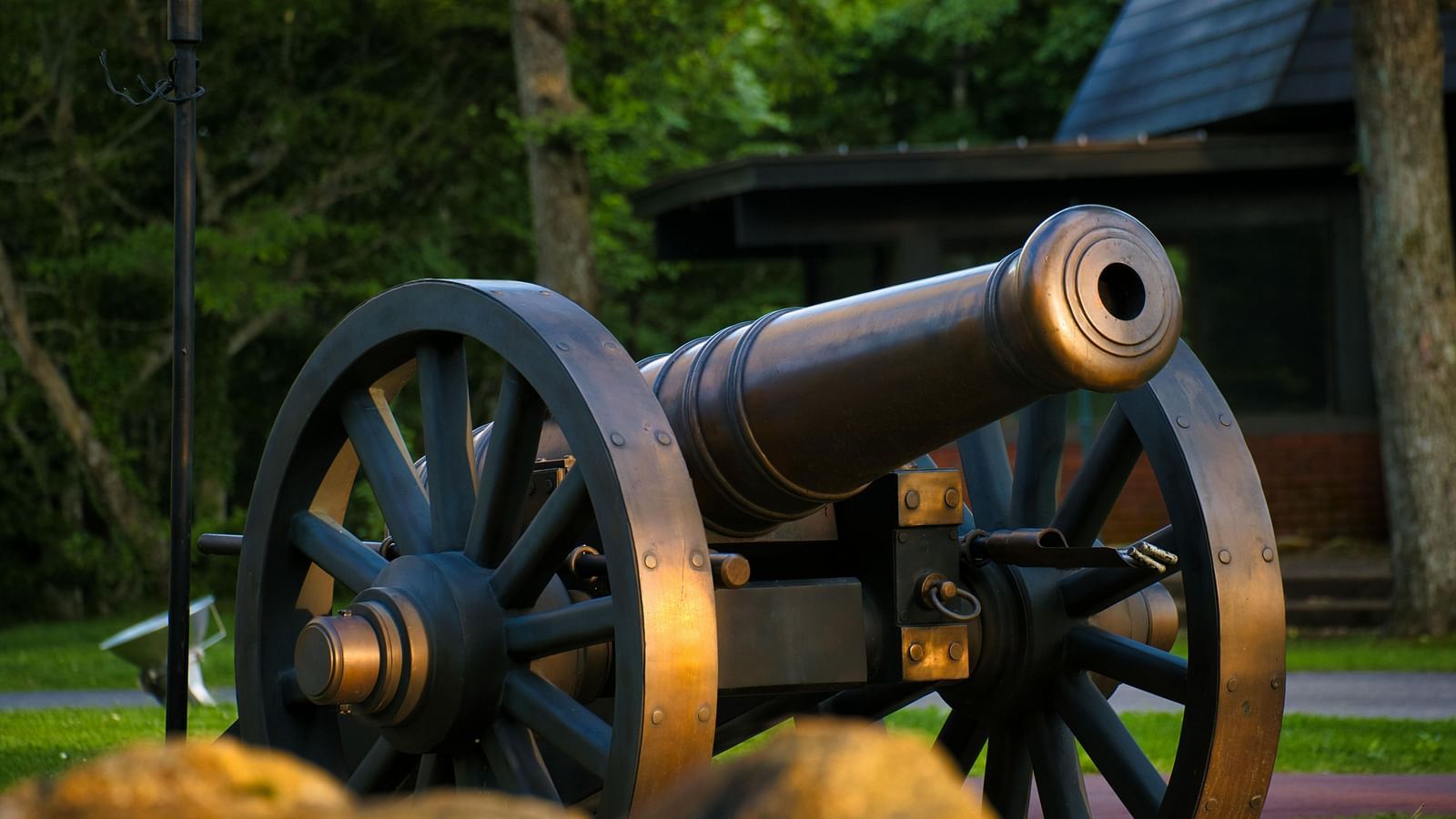 Old cannon displayed on a grassy field with trees in the background.