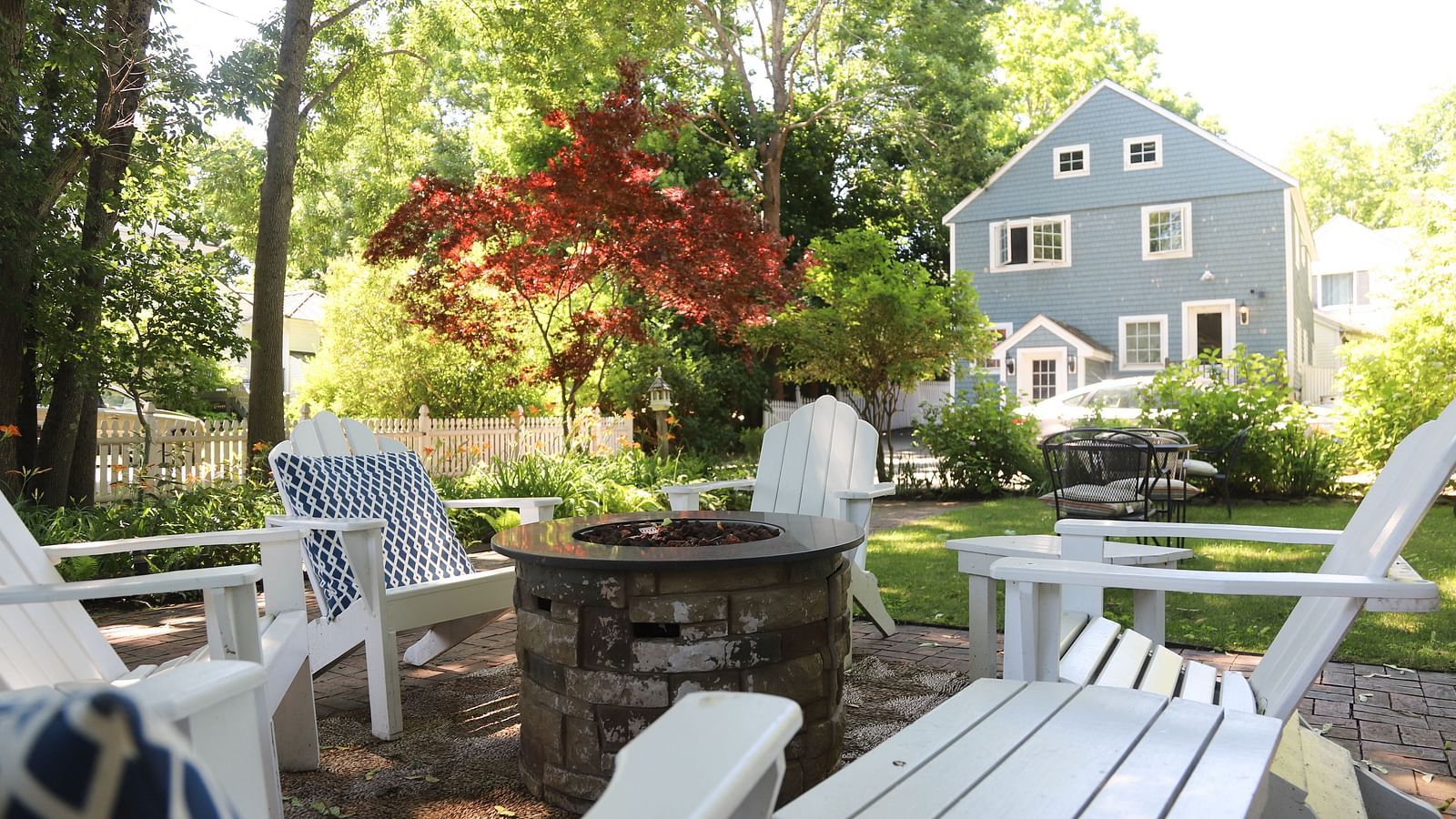 Outdoor garden seating area with white Adirondack chairs and a view of Hartstone Inn in the background.