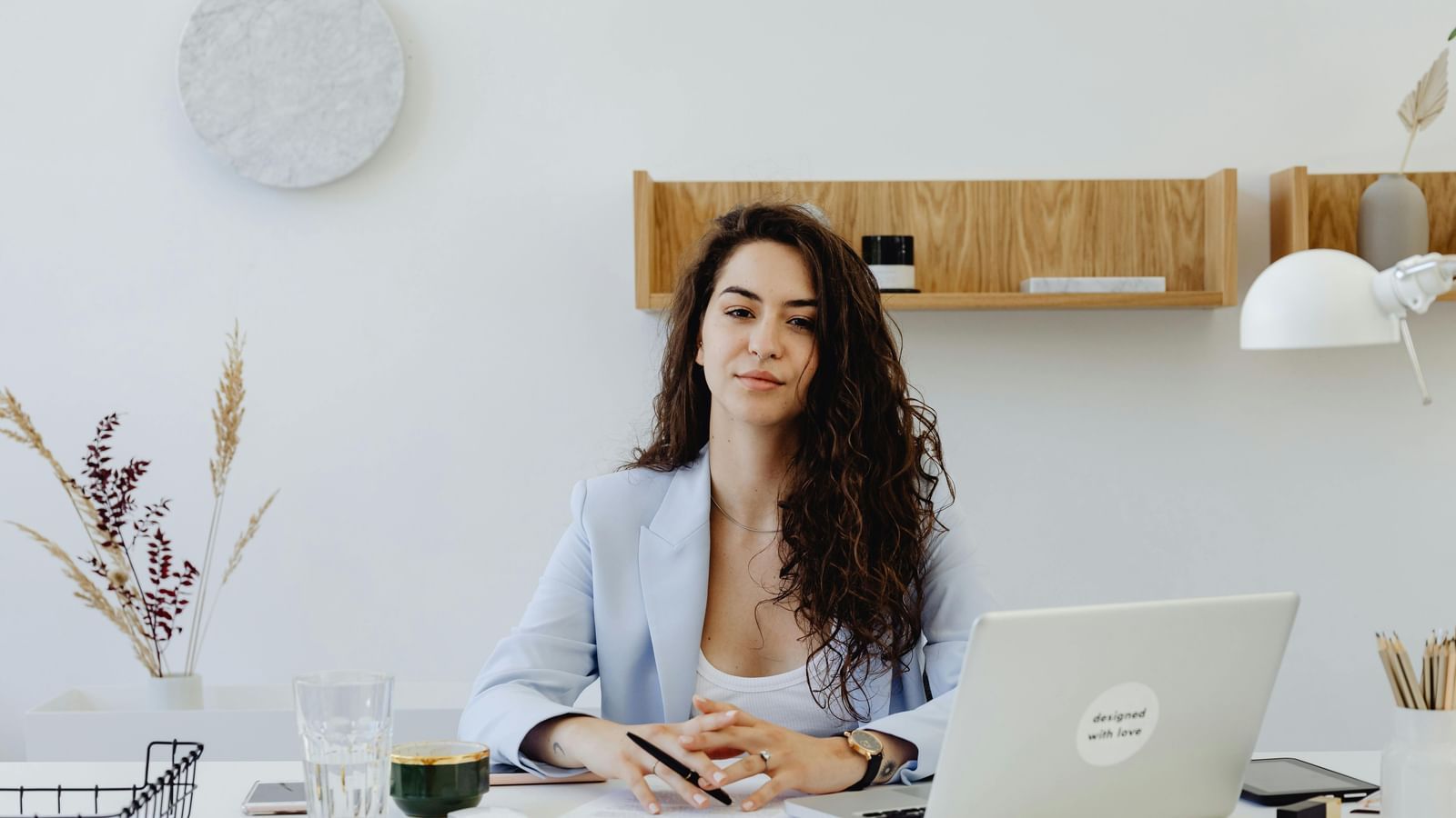 A businesswoman in a light blazer sitting at a desk with a laptop.