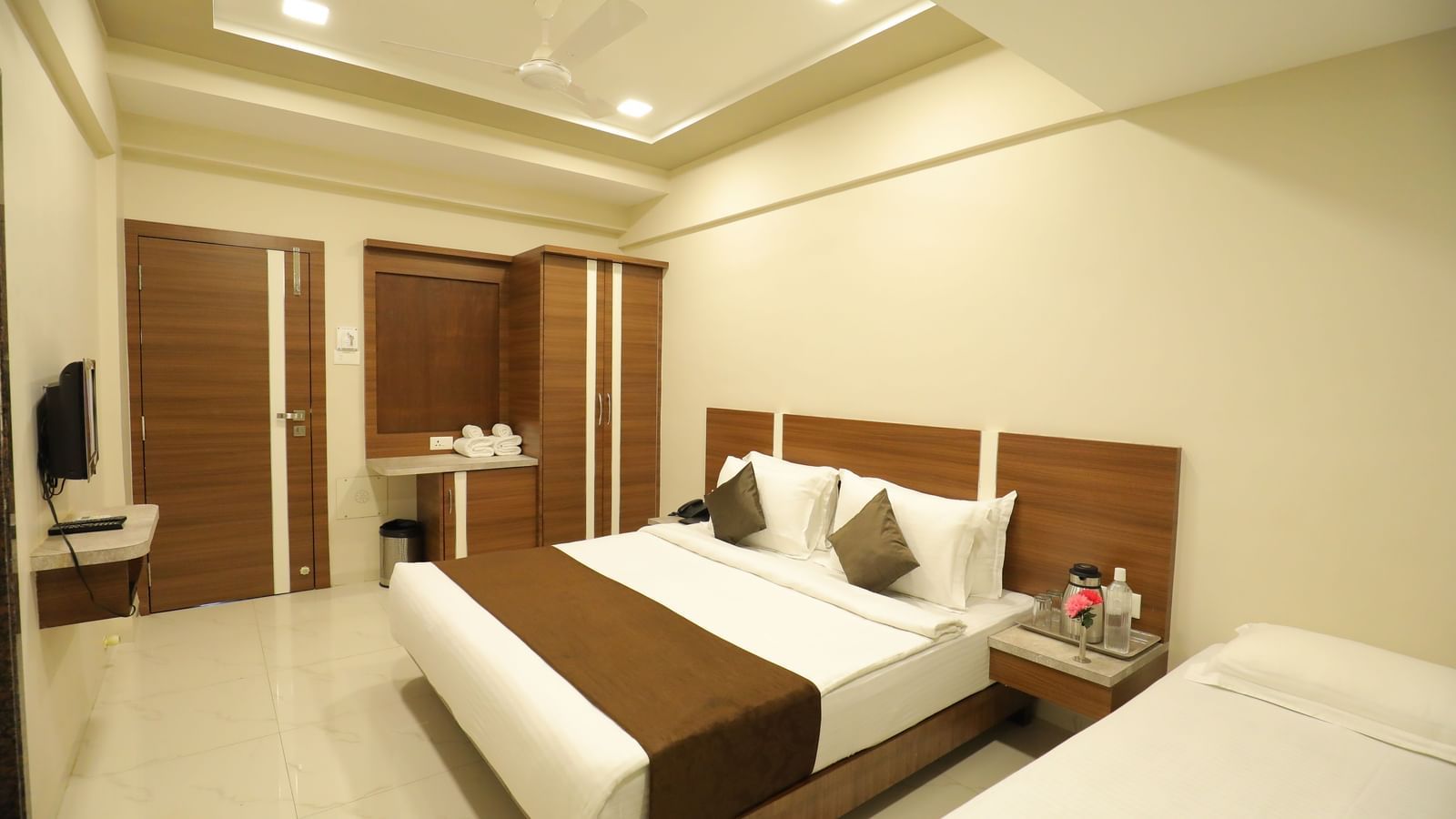 Extended view of the plush queen size bed in the Deluxe Room of the Highland Resort furnished with a wardrobe, wall-mounted TV, and bedside tables.