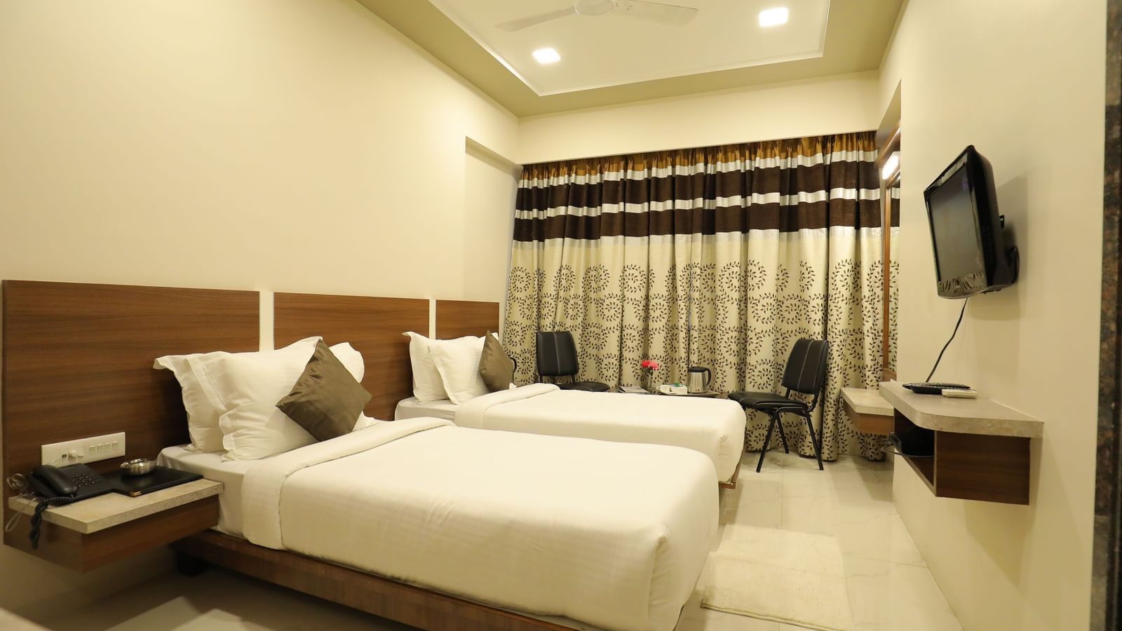 A Super Deluxe Room of Highland Resort furnished with twin beds, a wall-mounted TV, seating area for two, and closed curtains.