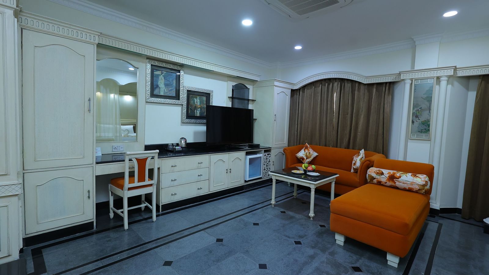 Wide angle image of a Suite at Amar Hotel with a sofa, table, TV and a curtains