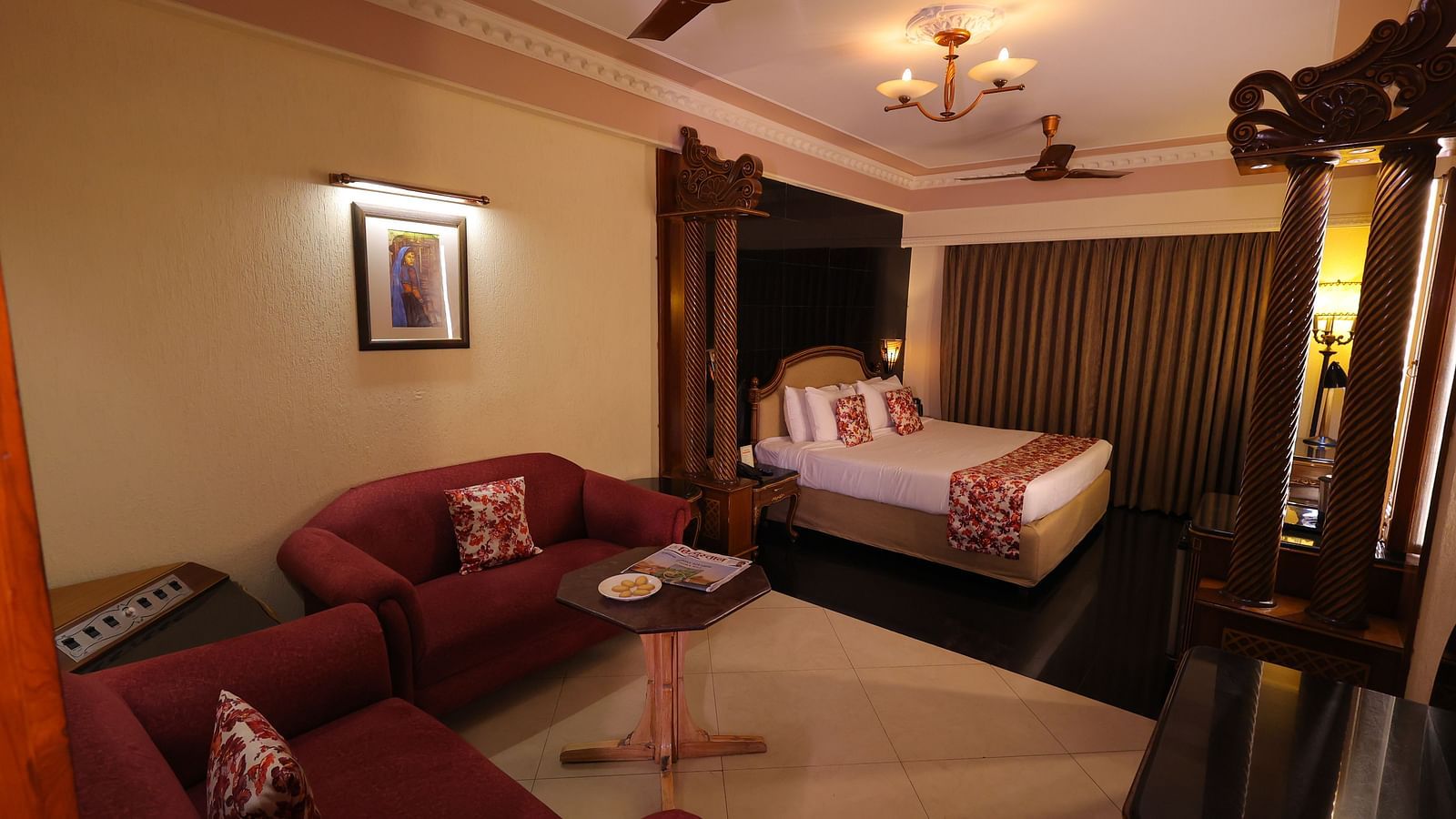 Overview image of Premium room at Hotel Amar with a bed, red sofa, table and long curtains.